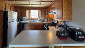 A compact kitchen with wooden cabinets, a stainless steel refrigerator, a stove, and a sink. - River House & Fishing (Elk River)