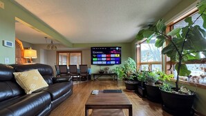 A living room with a leather sofa, a coffee table, a flat-screen TV, and potted plants. - River House & Fishing (Elk River)