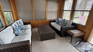 A cozy room with a sofa, a bench, and a coffee table. There are large windows with blinds, and a wicker chair is visible. - River House & Fishing (Elk River)