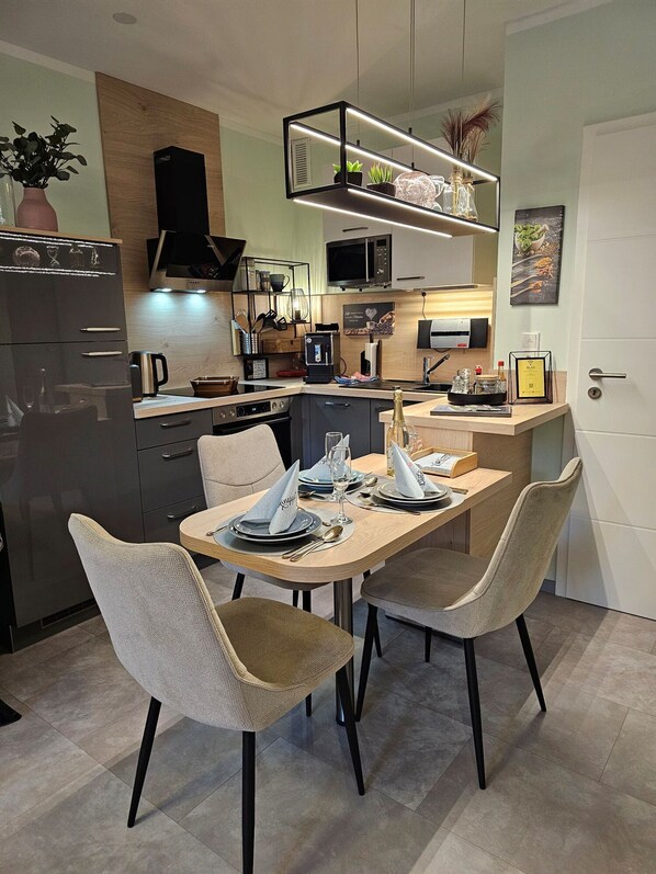 Une cuisine moderne avec un coin repas, comprenant une table dressée pour quatre personnes, un réfrigérateur, un four à micro-ondes et une machine à café.
