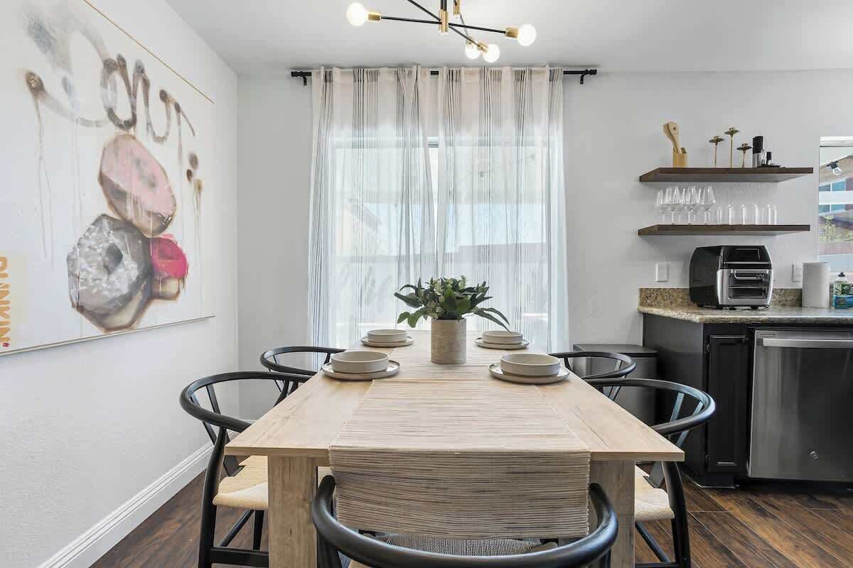 A modern kitchen with a wooden dining table, chairs, a coffee machine, and a refrigerator.