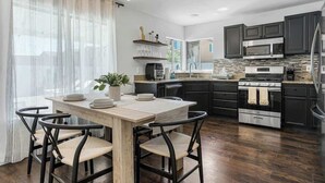 A modern kitchen with dark cabinets, a wooden dining table, and a chandelier.