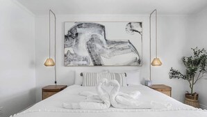 A bedroom with a large abstract painting, a swan-shaped towel arrangement, and two bedside lamps.