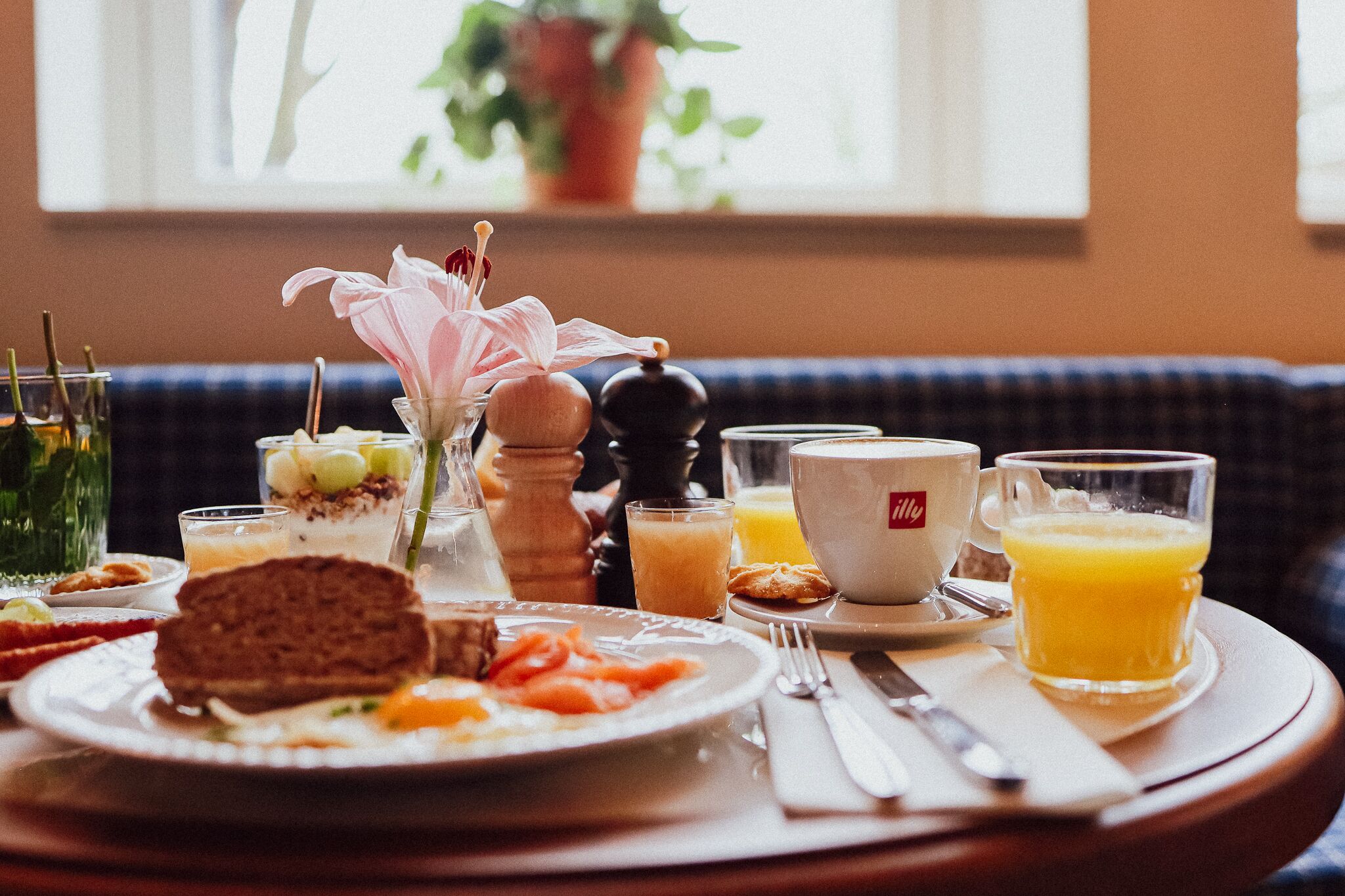 En morgenmadsbordopstilling med mad på en tallerken, et glas appelsinjuice og en kaffekop på bordet.