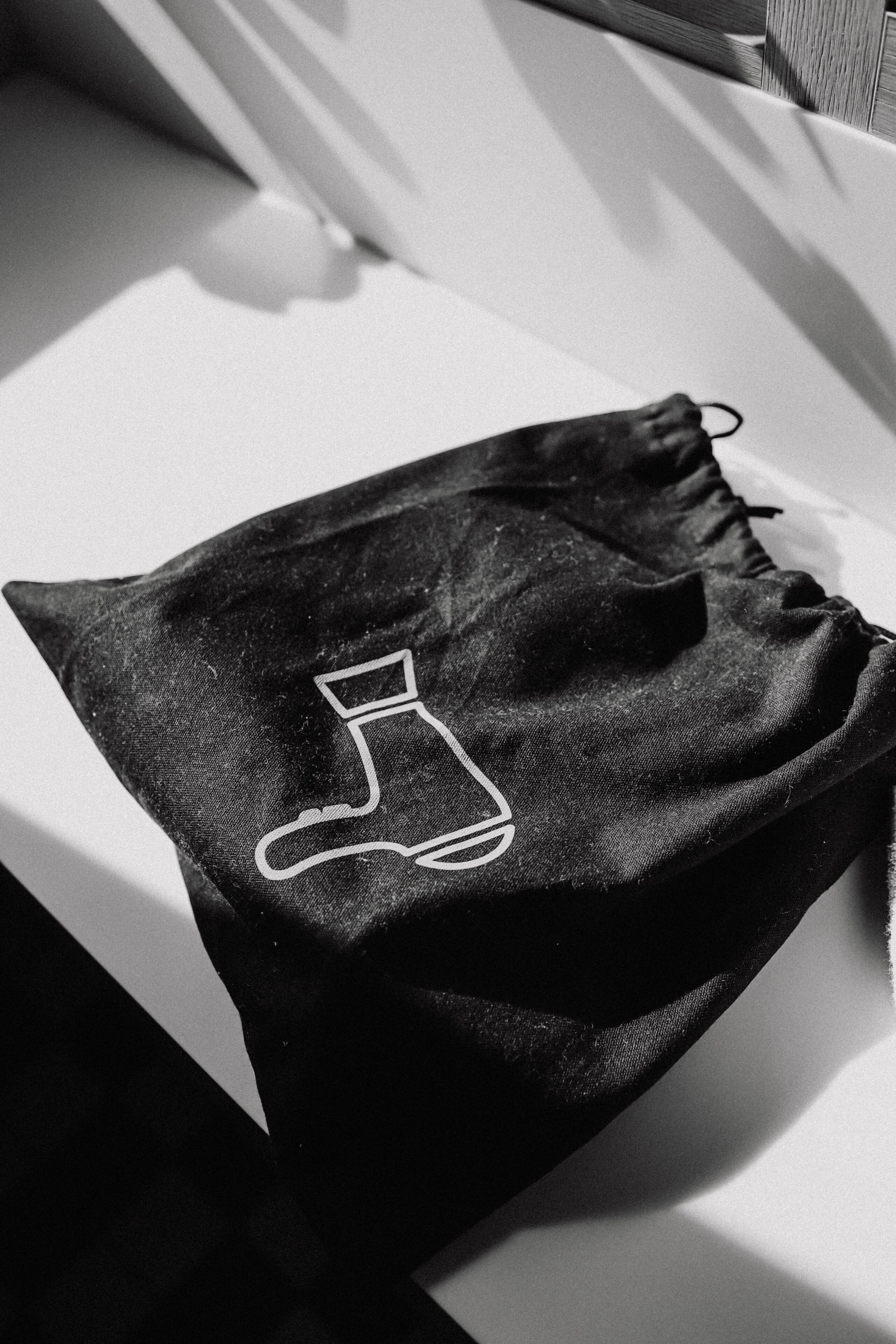 Una bolsa negra de cordón con un diseño bordado blanco sobre una superficie blanca.