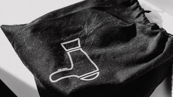 Una bolsa negra de cordón con un diseño bordado blanco sobre una superficie blanca.