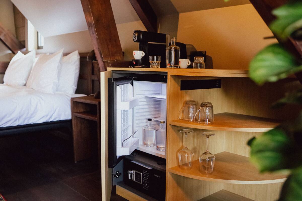 A compact room with a bed, a built-in refrigerator, and shelves with glassware.