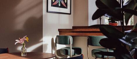 A room with a dining table, chairs, a framed artwork on the wall, a potted plant, and a window with a view.