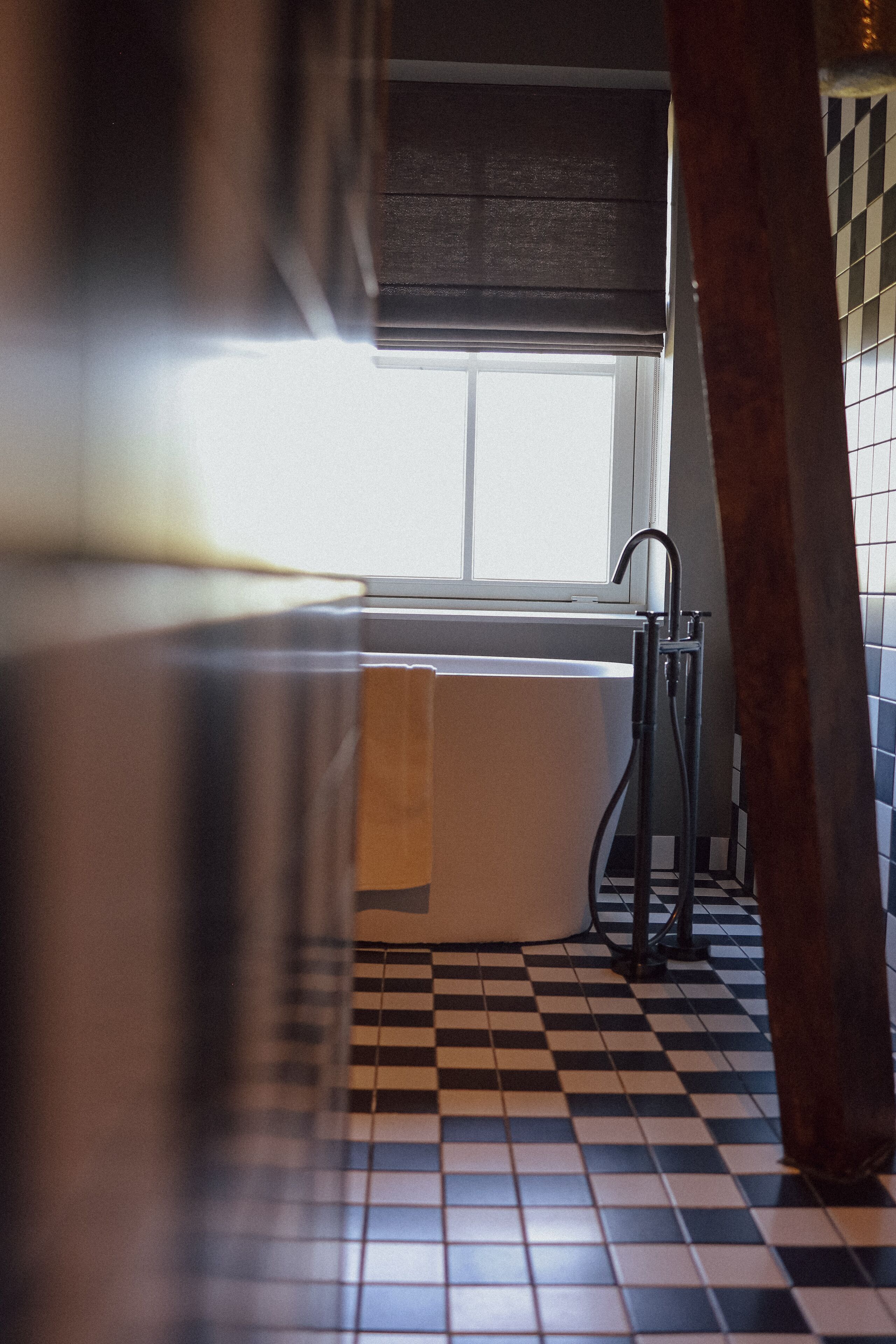 Een badkamer met een zwart-wit schakeerd patroon op de vloer, een badkuip en een raam met uitzicht.