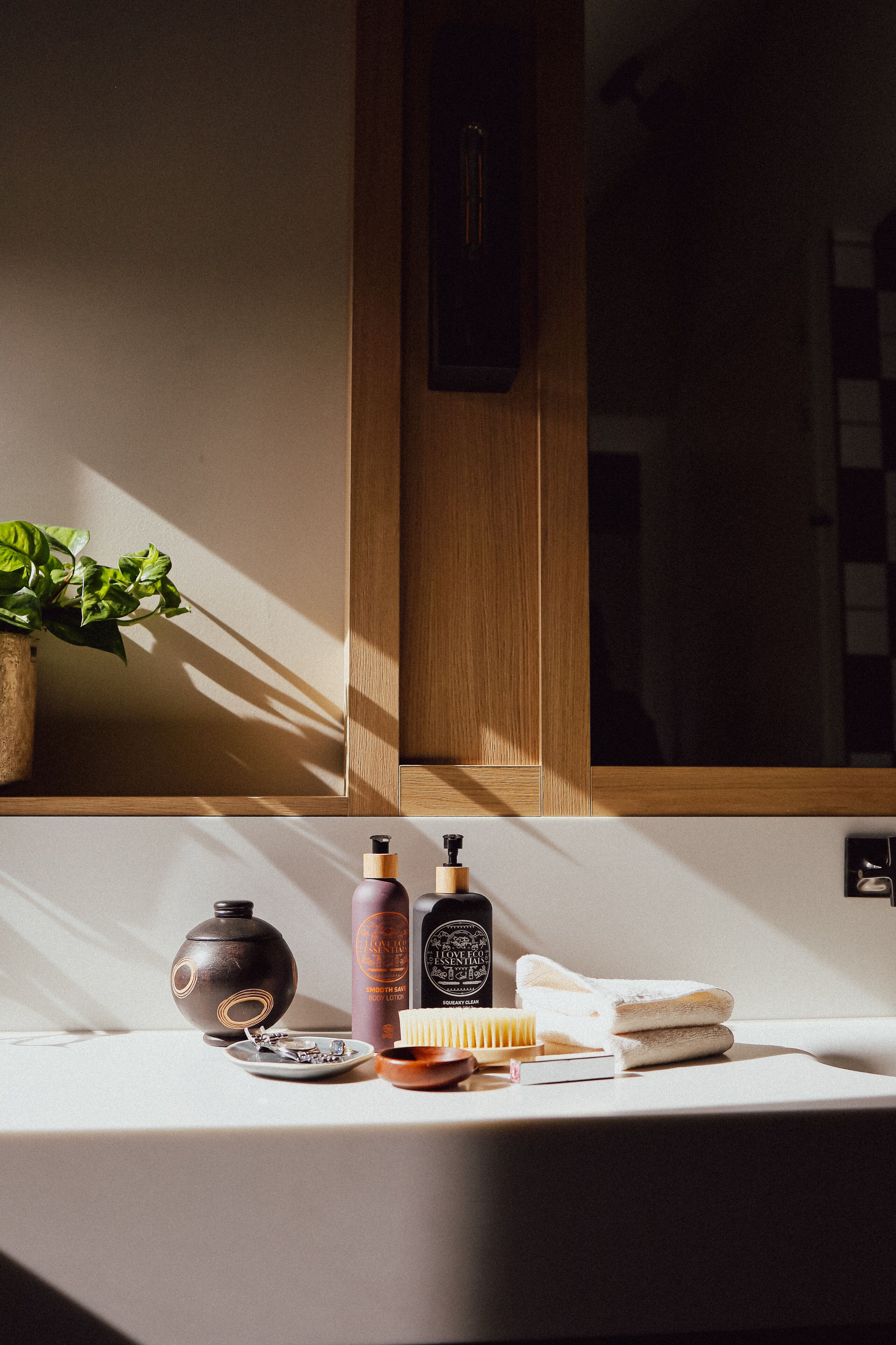 A bathroom vanity with a mirror, a potted plant, toiletries, and a towel.
