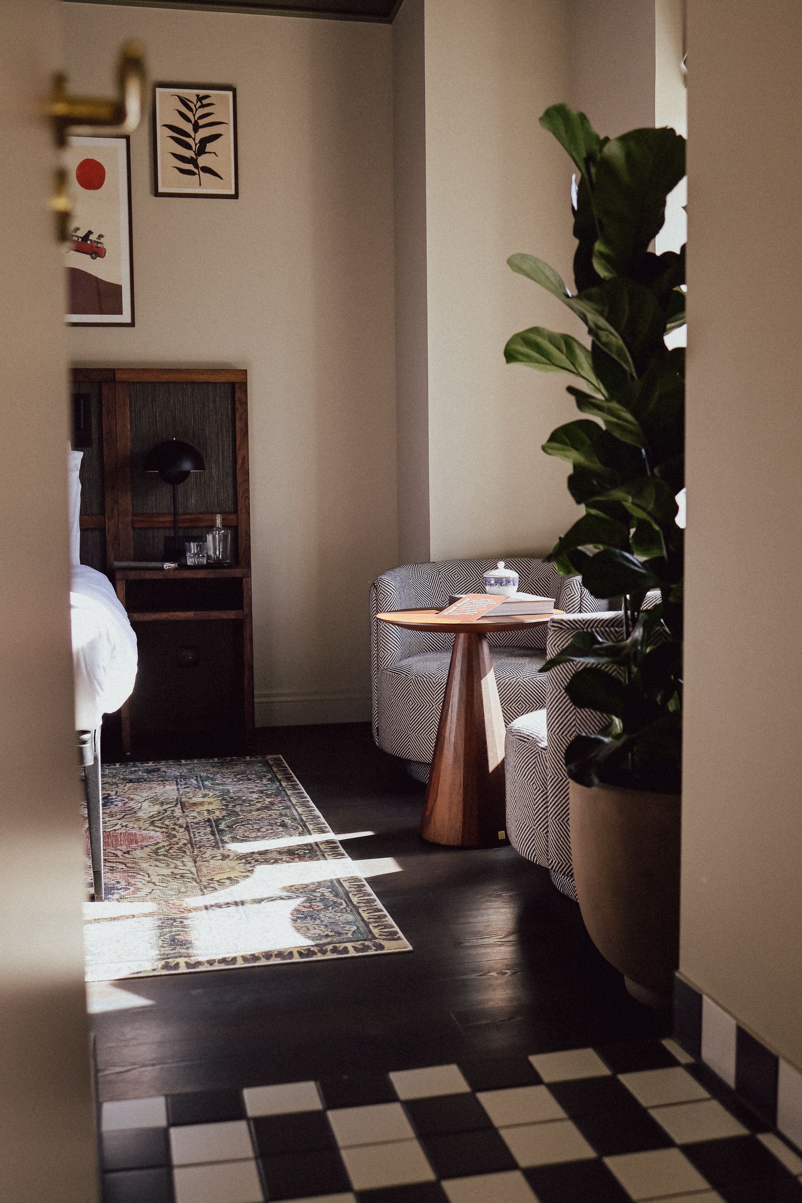 A hallway with a checkered floor, a sofa, a table with a plant, and artwork on the wall.