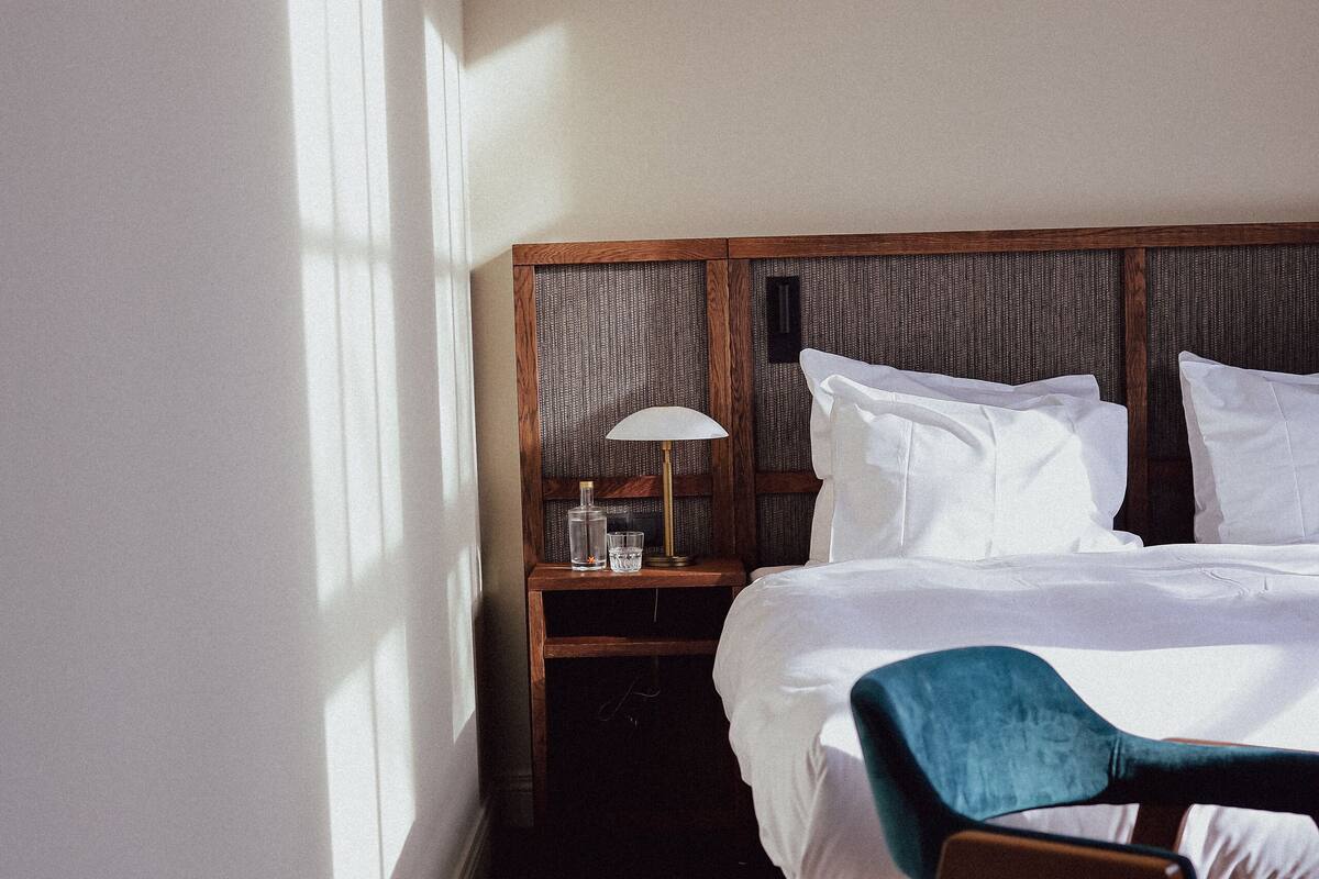 A hotel room with a bed, a nightstand with a lamp, a chair, and a patterned rug.