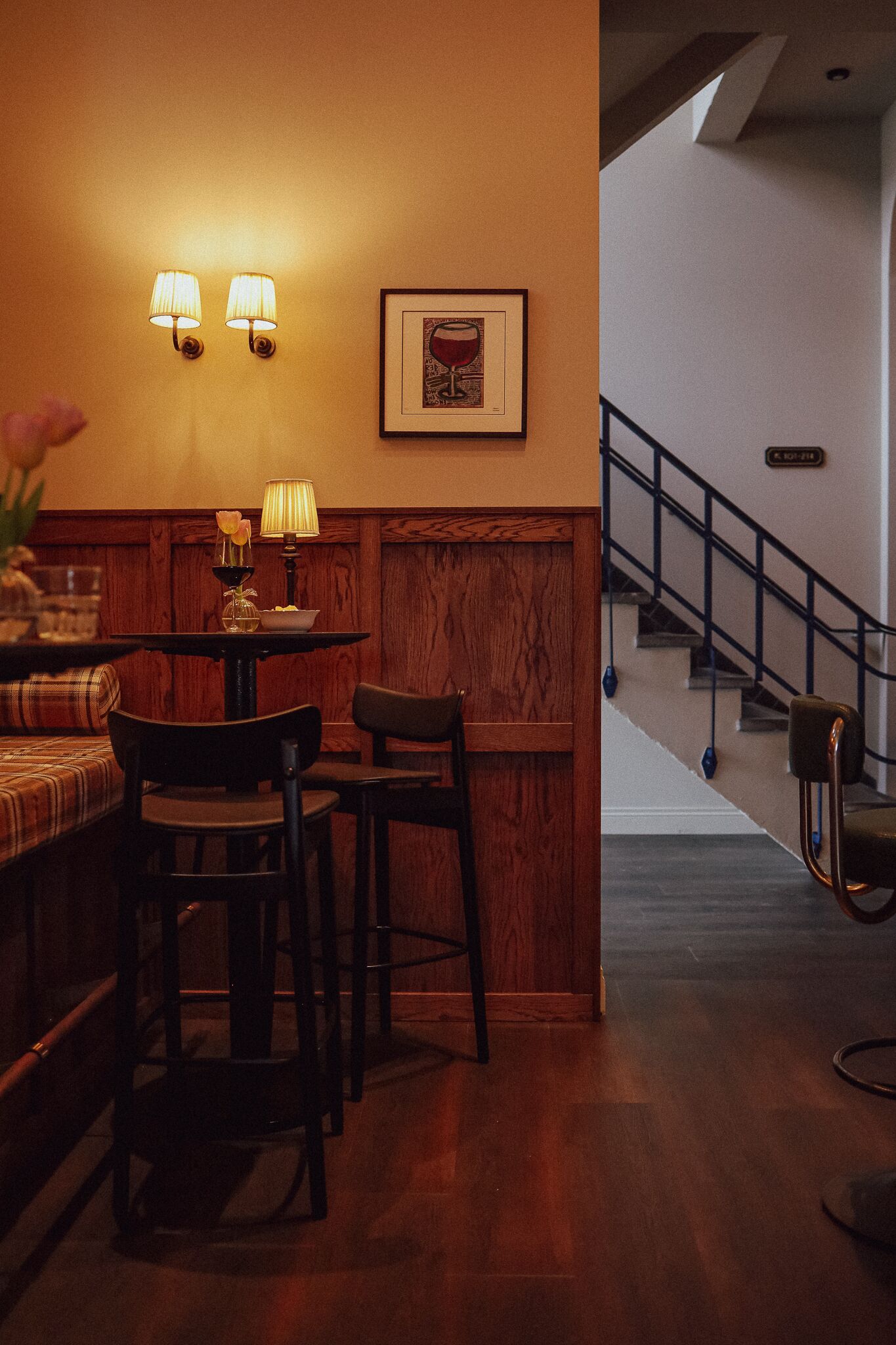 A cozy bar area with a wooden bench, two chairs, a table with a lamp, and a framed picture on the wall.