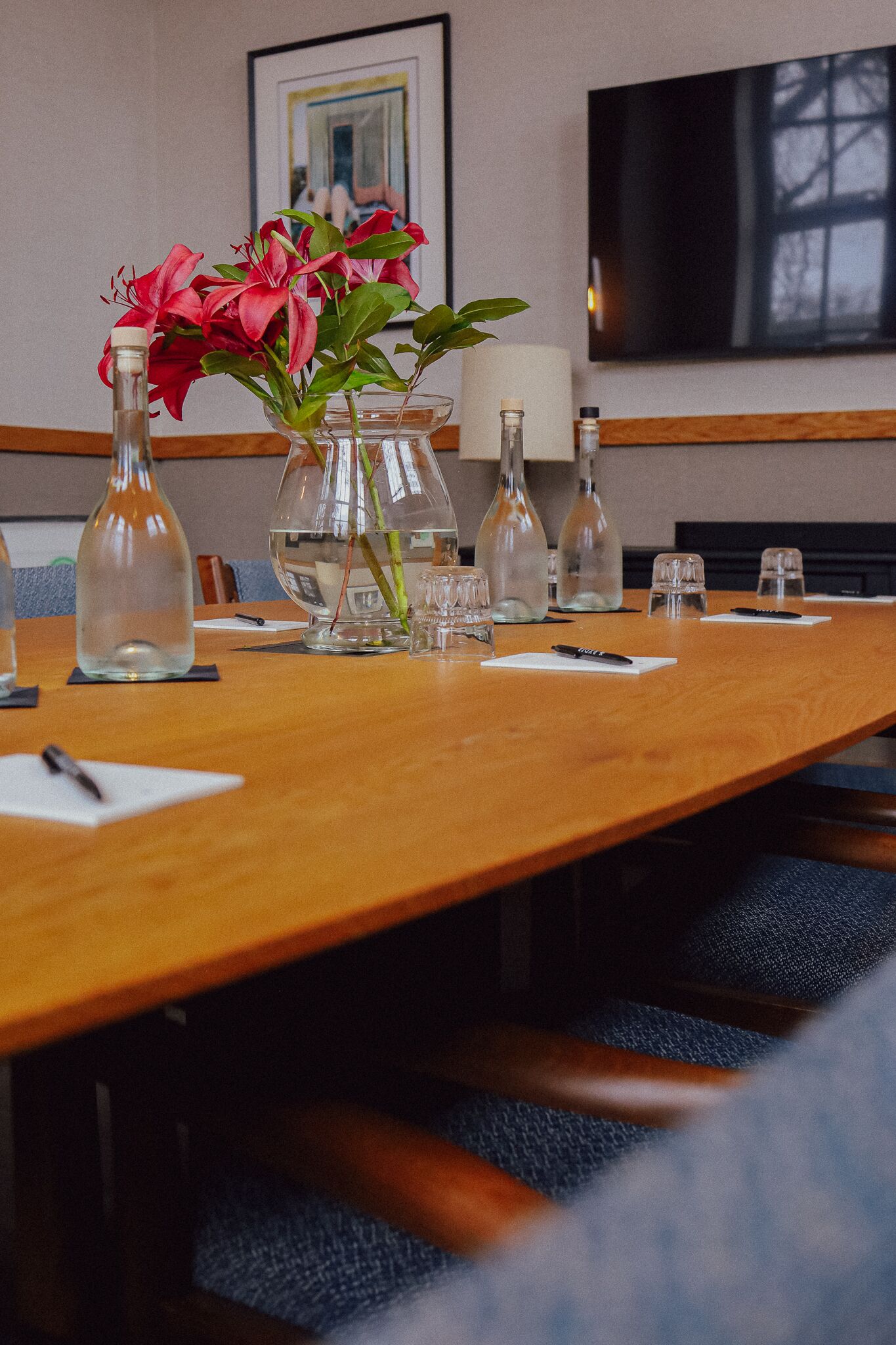 Una mesa de conferencias con jarrones de flores, vasos de agua y un control remoto.