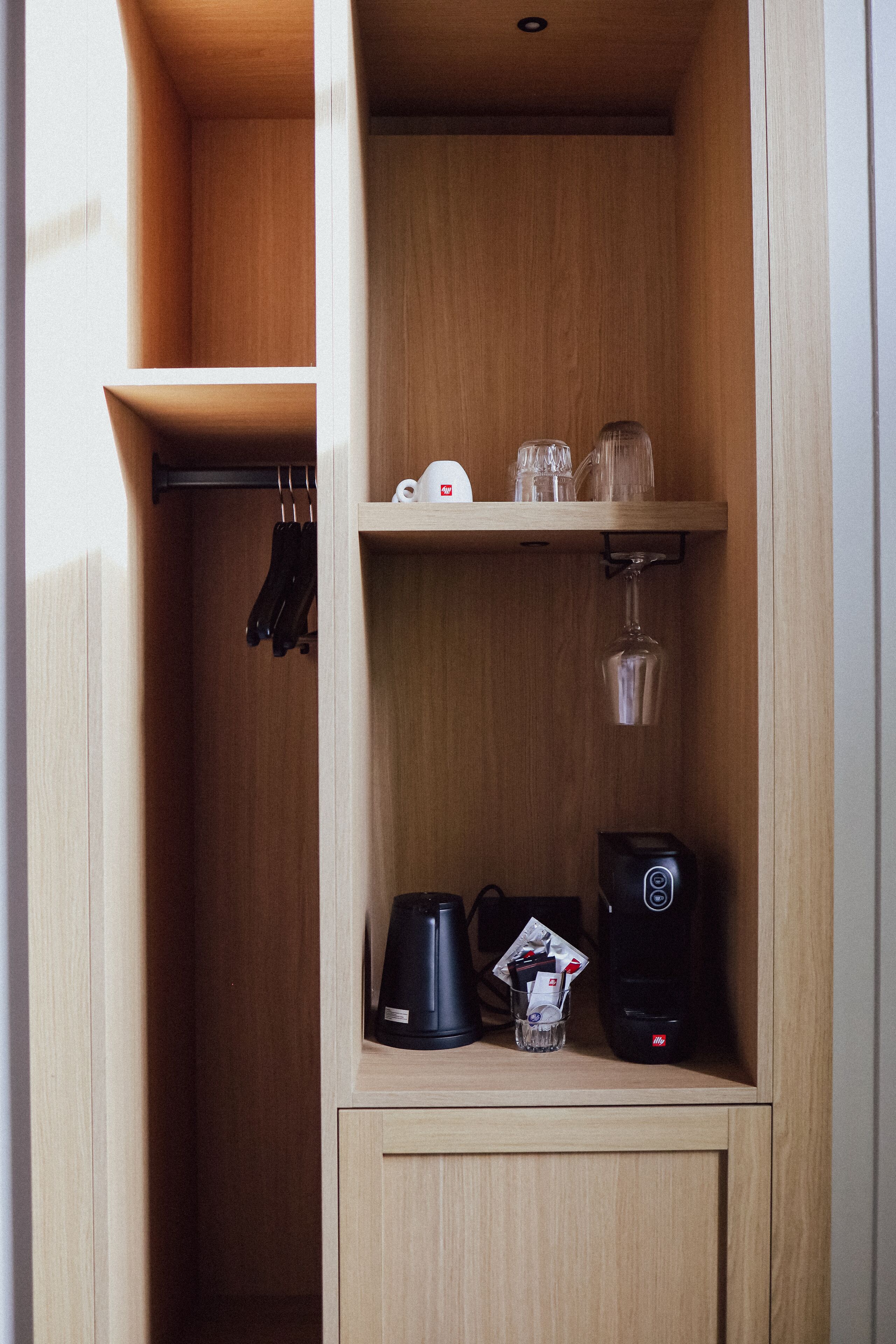 Una kitchenette compacta con cafetera, tostadora y un vaso de agua sobre la encimera.