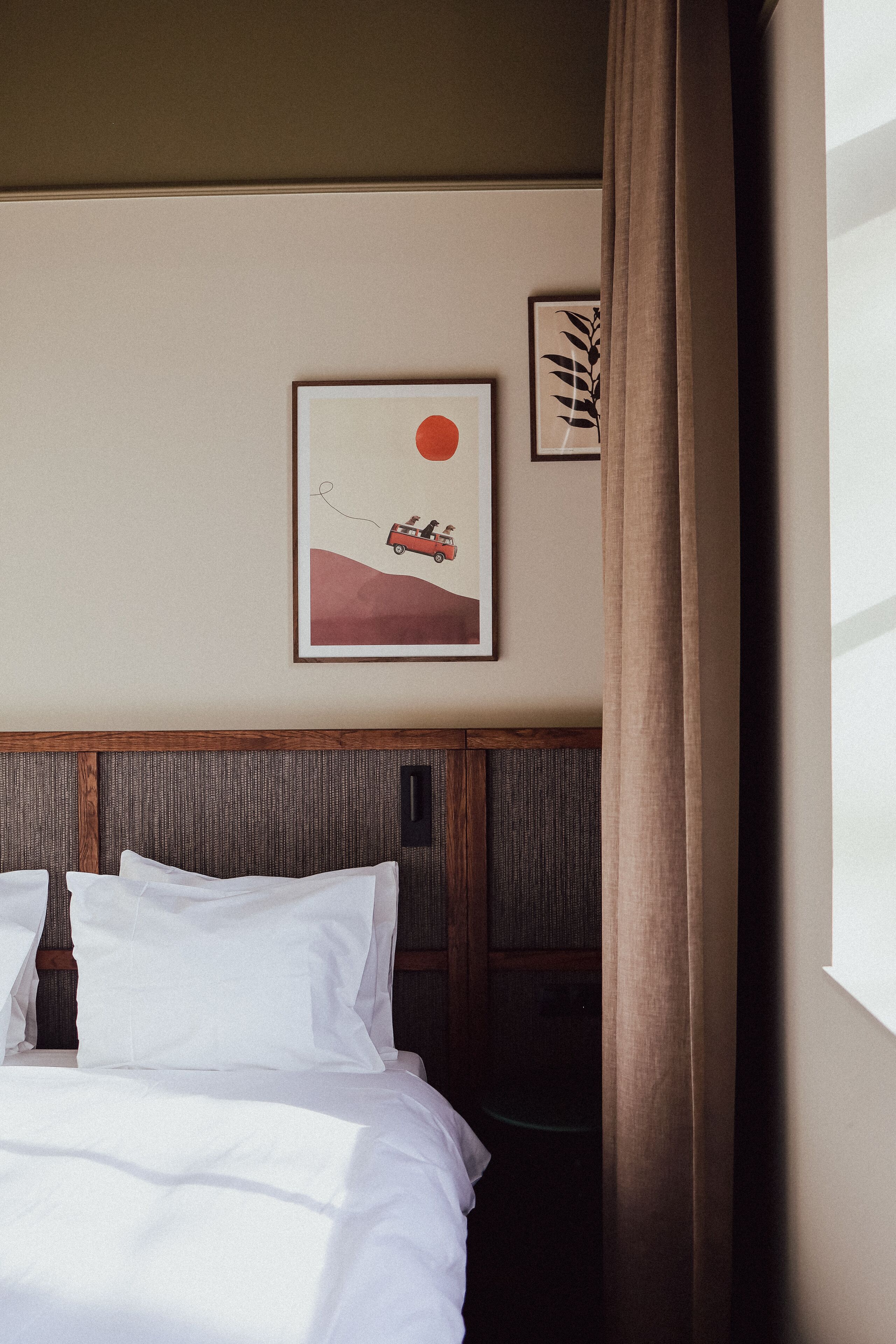 Een hotelkamer met een bed, hoofdbord, een aan de muur hangend schilderij en een gordijn.