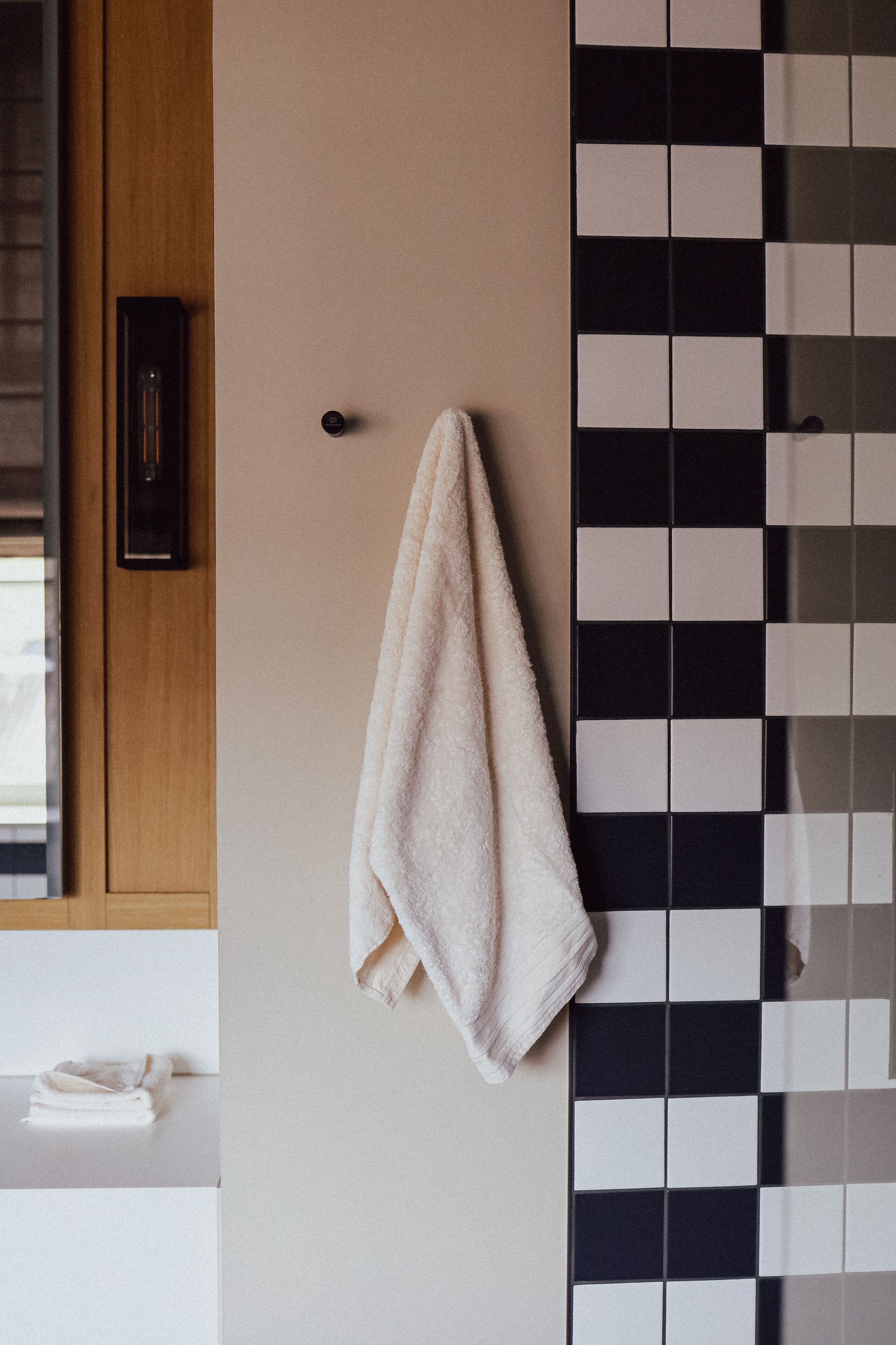 Un baño con una toalla colgada en un perchero, un mueble de madera y una pared con baldosas blanco y negro.