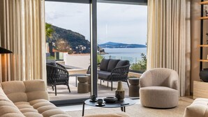 A modern living room with a sofa, armchairs, and a coffee table. A large window offers a view of the sea and hills. - Majestic Villa Lidija w/ private infinity pool and sea view  (Dubrovnik)