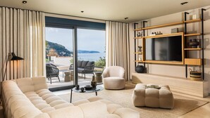 A modern living room with a sofa, ottoman, and a flat-screen TV on a wooden shelf. - Majestic Villa Lidija w/ private infinity pool and sea view  (Dubrovnik)