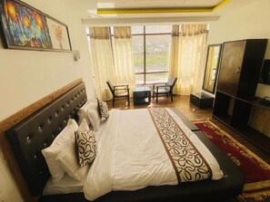 A hotel room with a large bed, a TV, a desk, and a window with curtains. - Hotel The White Castle (Kargil)