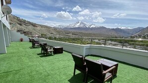 A rooftop terrace with green artificial grass, wooden furniture, and a view of snow-capped mountains. - Hotel The White Castle (Kargil)