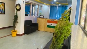 A reception area with a wooden desk, a black sofa, and a potted plant. - Hotel The White Castle (Kargil)