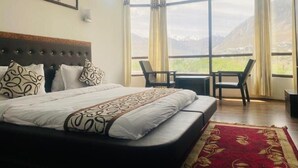 A hotel room with a large bed, a view of mountains through the windows, and a balcony with chairs. - Hotel The White Castle (Kargil)