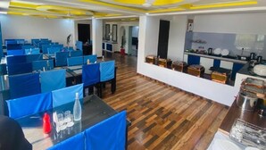 A modern dining area with blue chairs and tables, wooden flooring, and a central island with kitchen appliances. - Hotel The White Castle (Kargil)