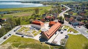 An aerial view of a town with a central building complex, surrounded by residential houses, a road, and a body of water in the background.