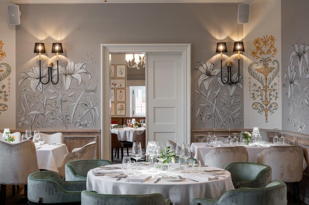 A dining area with round tables set for service, wall-mounted light fixtures, and floral wall art.
