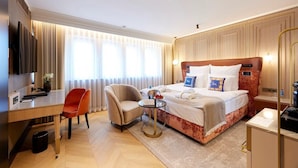 A hotel room with a bed, a desk, a chair, a small table, and a TV.