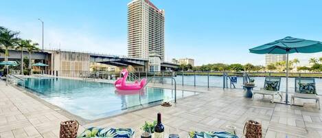 A rooftop pool area with lounge chairs, a pink flamingo float, and a bottle of wine on a tray.