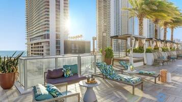A rooftop terrace with outdoor seating, palm trees, and high-rise buildings in the background.