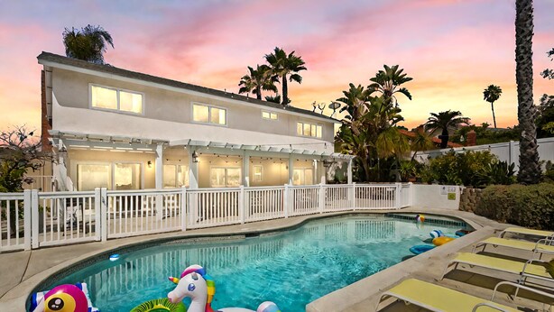 A swimming pool with inflatable toys, a white building with multiple windows, and a white fence. - Stunning Coastal Escape w. private pool & spa, arcade, near themed parks & beach (Mission Viejo)