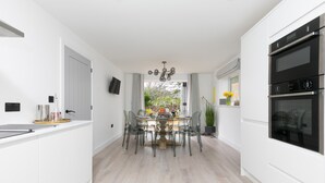 A modern kitchen with white cabinetry, a dining area with clear chairs, and a large oven.
