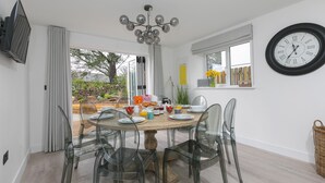 A dining area with a round table, clear chairs, a chandelier, and a wall clock.
