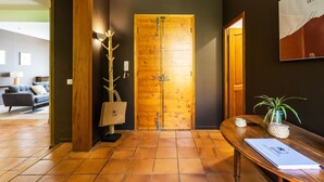Une porte en bois avec une poignée en métal, un banc en bois agrémenté d’une plante et un luminaire fixé au mur.