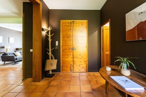 Een houten deur met een metalen hendel, een houten bankje met een plant, en een wandlamp.