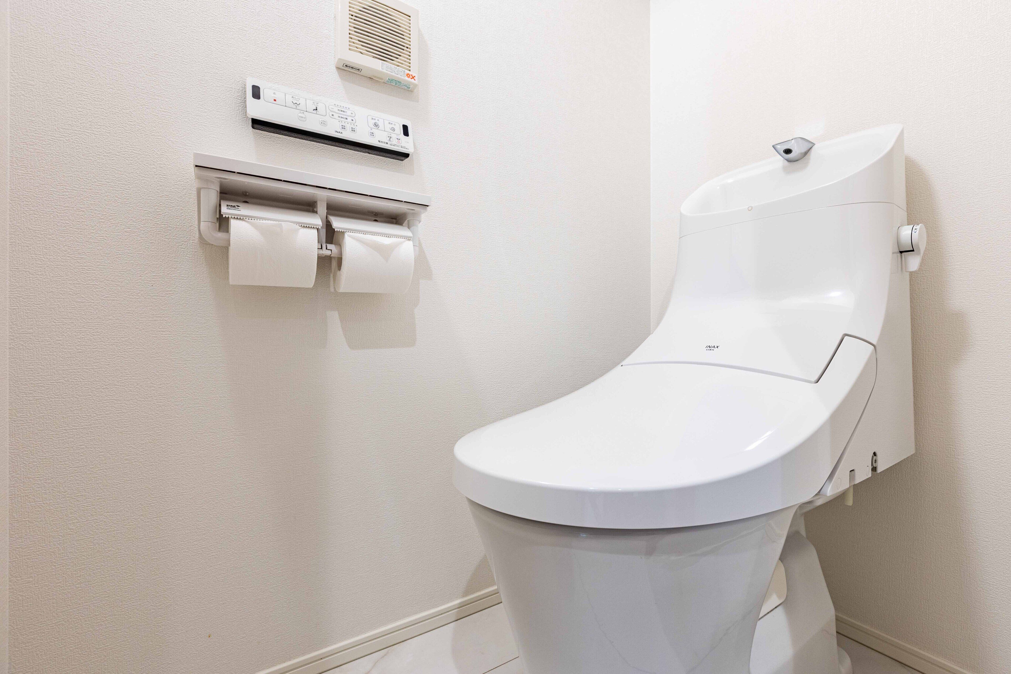 A modern bathroom with a white toilet, a wall-mounted air purifier, and a paper towel dispenser.