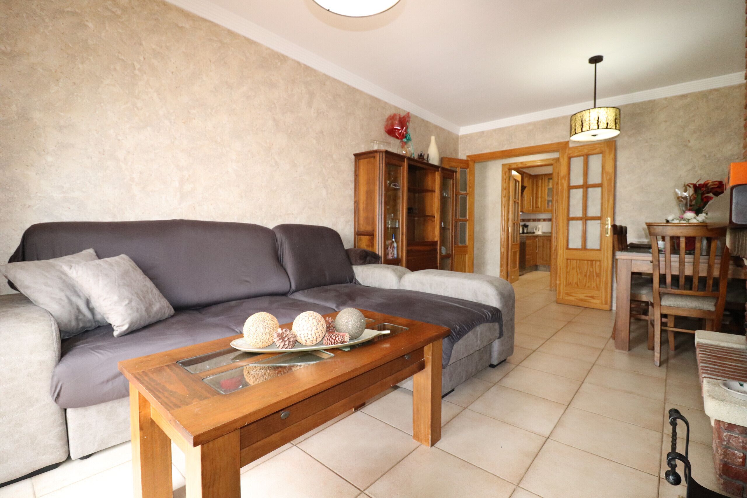 Un salon comprenant un canapé, une table basse en bois agrémentée d’objets décoratifs, un meuble et un coin repas avec une chaise et une table.