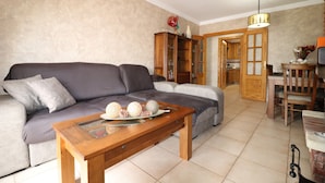 A living room with a sofa, a wooden coffee table with decorative items, a cabinet, and a dining area with a chair and table. - 1020 Casa Pat (Nerja)