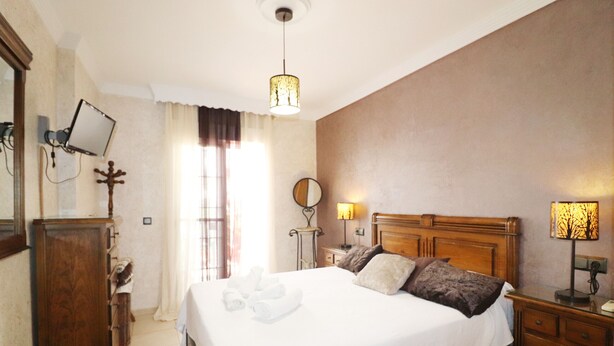 A neatly arranged bedroom with a large bed, bedside lamps, a wooden dresser, and a mirror on the wall. - 1020 Casa Pat (Nerja)