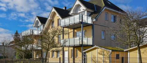 Un edificio residenziale a più piani con un balcone, un cortile recintato e un cielo sereno.