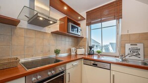 Una cocina moderna con horno empotrado, microondas y lavavajillas, encimeras de madera y una ventana con persianas.