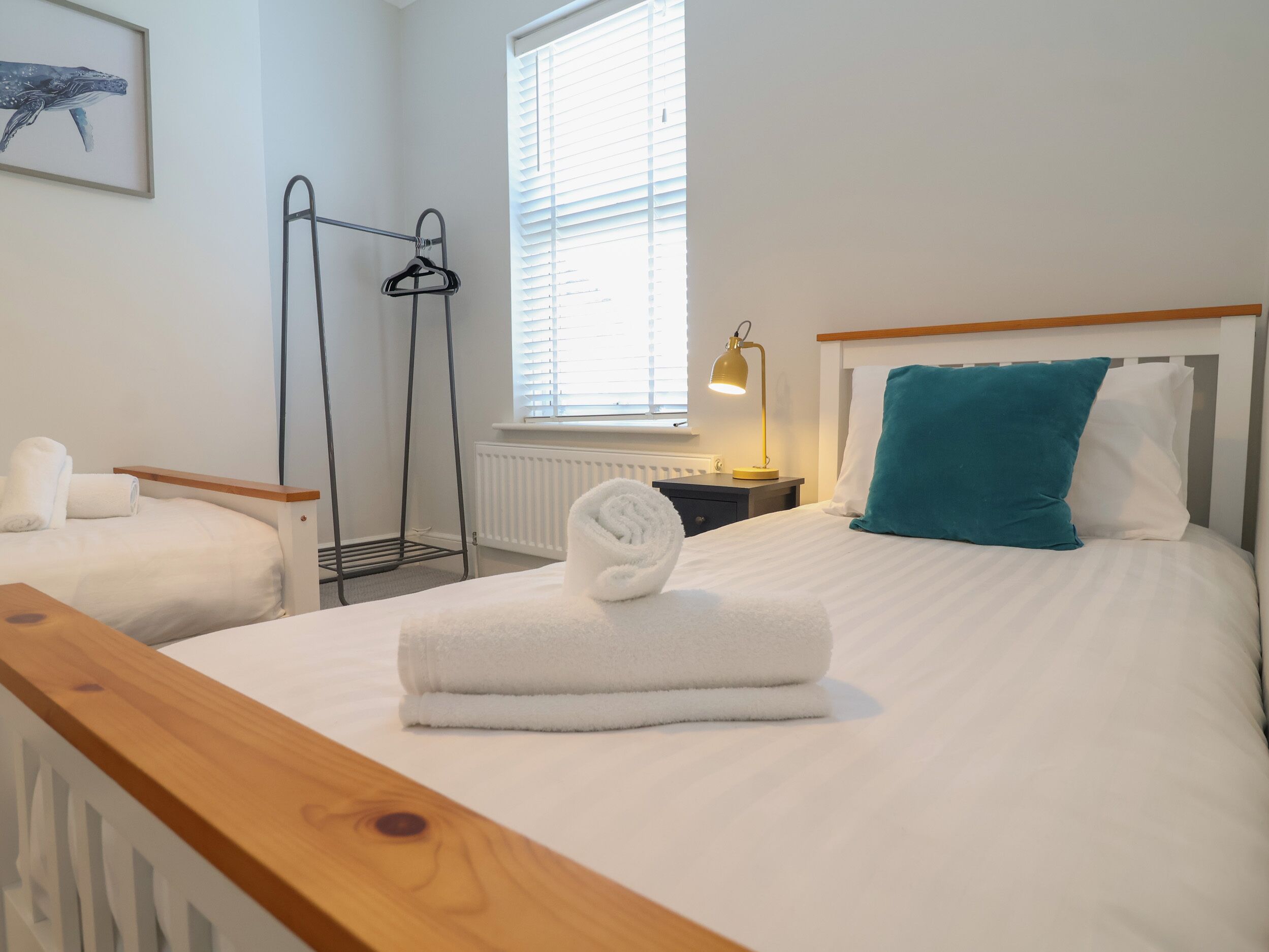 A hotel room with two beds, a radiator, a window with blinds, a hanging clothes rack, and a bedside lamp.