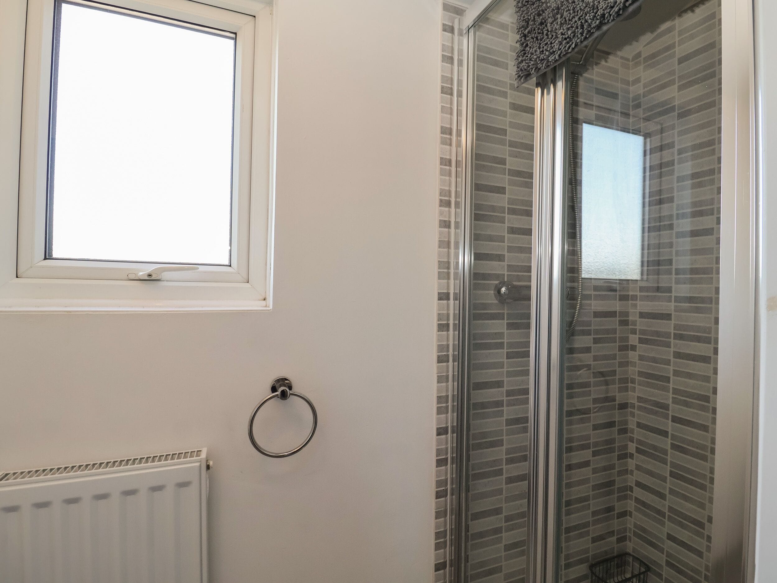 Un baño con ventana, un perchero para toallas y una ducha con puerta de cristal.