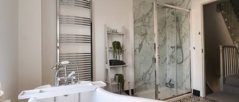 A modern bathroom with a freestanding bathtub, a glass-enclosed shower, and marble walls.