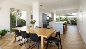 A modern kitchen with a central island, a dining area with a wooden table and black chairs, and a view of the outdoors through large sliding doors.