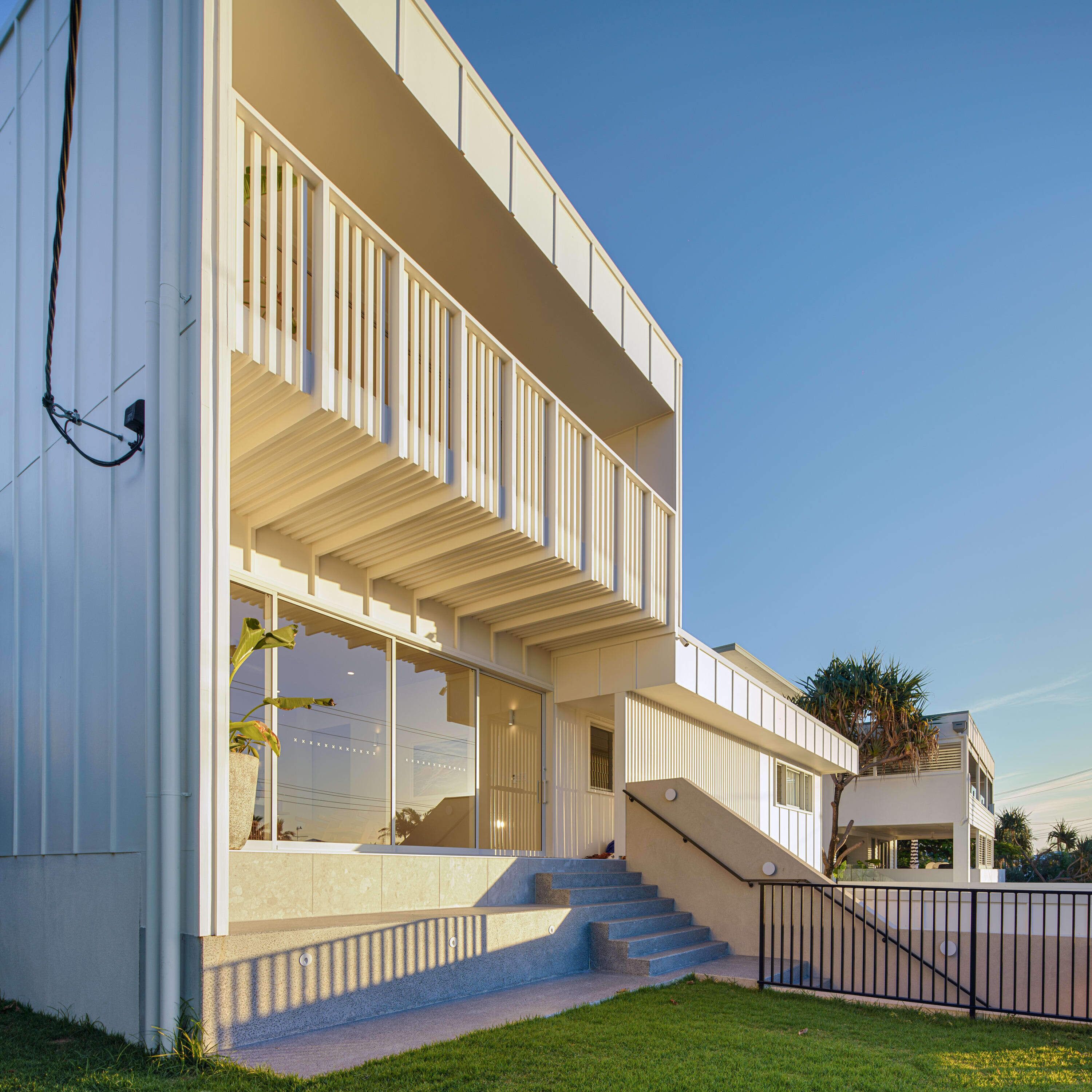 Un bâtiment moderne à deux étages, doté d’un toit plat, de grandes fenêtres et d’un escalier menant à l’entrée.