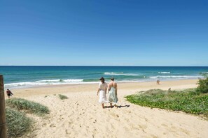 Una playa arenosa con olas del océano, cielo despejado y una pareja caminando.